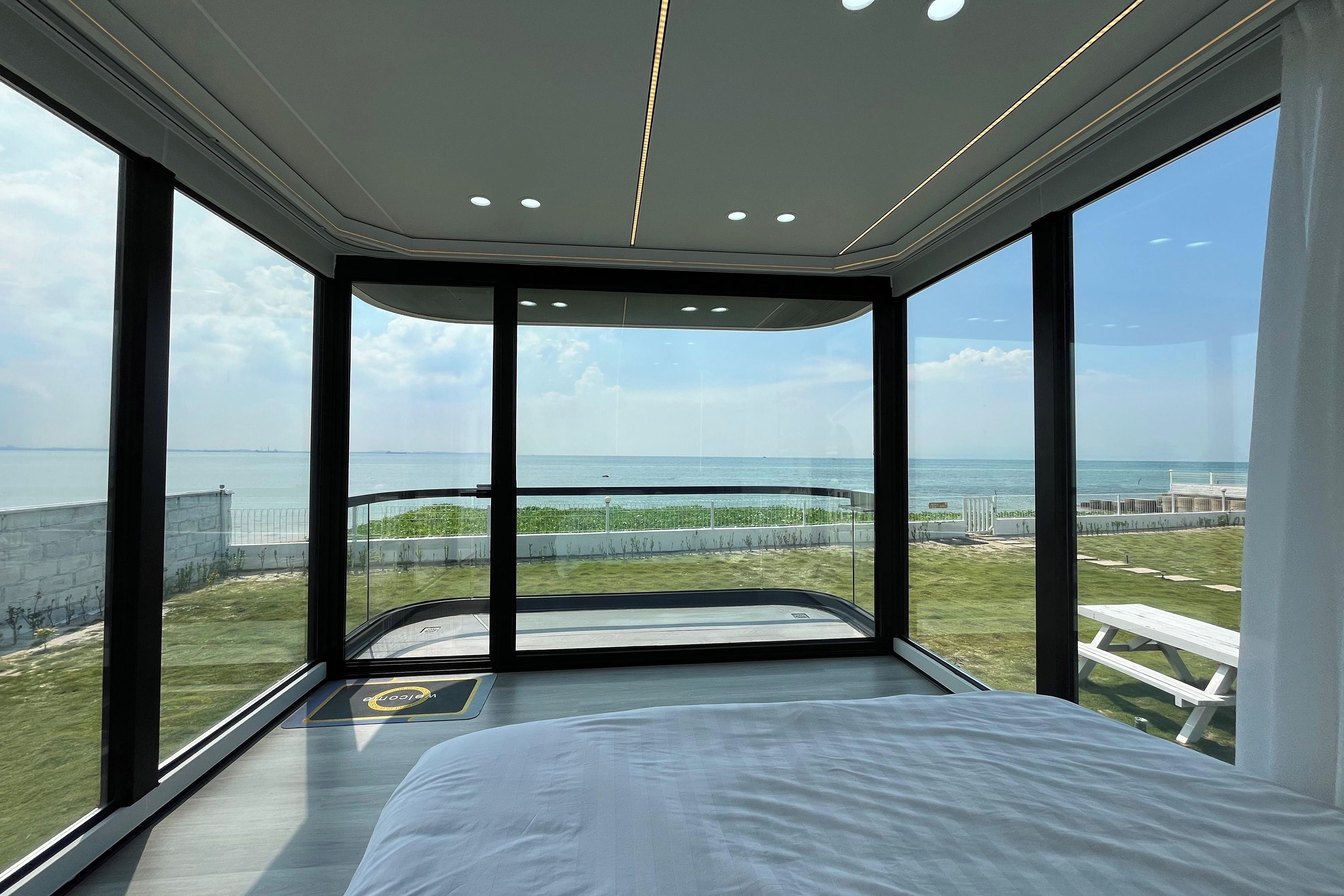 A modern bedroom with a large bed, a view of the beach, and a balcony with a glass wall.