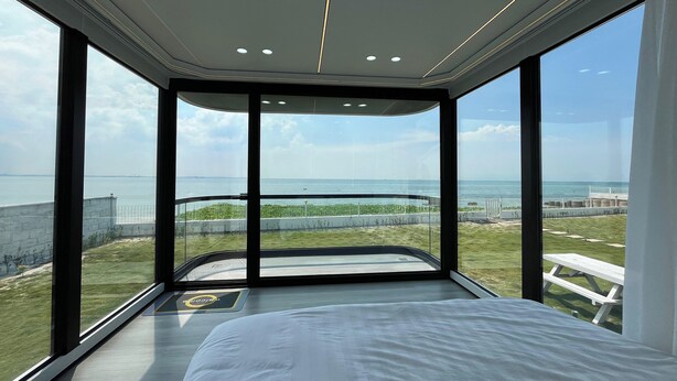 A modern bedroom with a large bed, a view of the beach, and a balcony with a glass wall. - Saga Village Hotel & Resort Bintan By Zuzu (Bintan)
