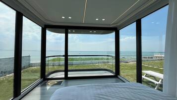 A modern bedroom with a large bed, a view of the beach, and a balcony with a glass wall.