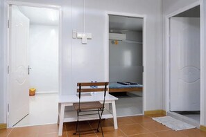 A small, clean room with a white table and chair, a bed, and a wardrobe. - Saga Village Hotel & Resort Bintan By Zuzu (Bintan)