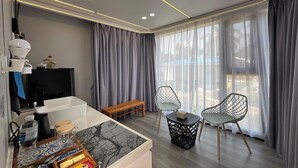 Une chambre moderne avec un banc en bois, deux chaises, une petite table, une machine à café et un téléviseur posé sur un meuble.