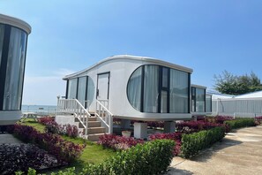 A modern, single-story mobile home with large windows and a covered outdoor area, surrounded by well-maintained gardens. - Saga Village Hotel & Resort Bintan By Zuzu (Bintan)
