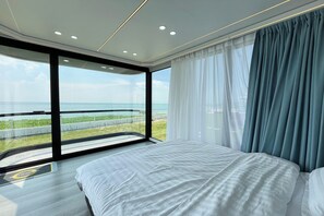 A modern bedroom with a large bed, a view of the sea, and a balcony. - Saga Village Hotel & Resort Bintan By Zuzu (Bintan)