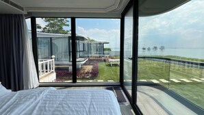 A modern hotel room with a large bed, a balcony with a view of the sea, and a glass wall. - Saga Village Hotel & Resort Bintan By Zuzu (Bintan)