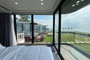 A modern hotel room with a large bed, a balcony with a view of the sea, and a glass wall. - Saga Village Hotel & Resort Bintan By Zuzu (Bintan)