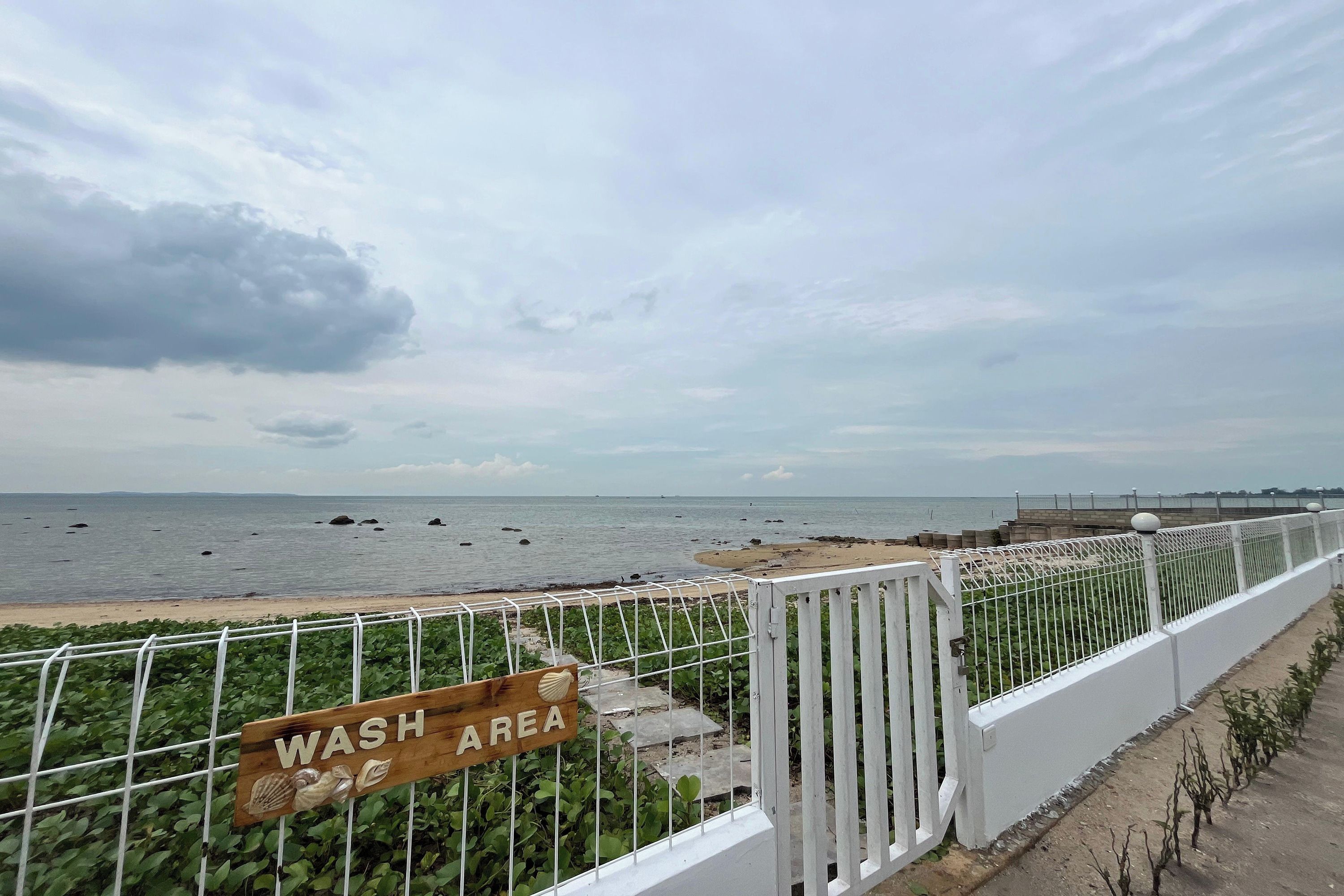 A coastal view with a 'WASH AREA' sign, a white fence, and a beach in the background.