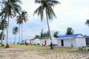 A row of white buildings with red doors, surrounded by palm trees and a sandy area. - Saga Village Hotel & Resort Bintan By Zuzu (Bintan)