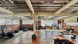 Une salle de sport équipée de divers appareils d’exercice, dotée d’un sol en béton et de murs en briques.