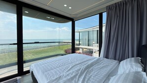 A modern bedroom with a large bed, a view of the sea, and a balcony with a glass railing. - Saga Village Hotel & Resort Bintan By Zuzu (Bintan)