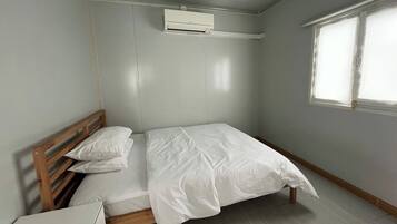 A small, clean room with a single bed, a bedside table, an air conditioning unit, and a window.