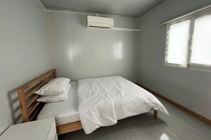 A small, clean room with a single bed, a bedside table, an air conditioning unit, and a window. - Saga Village Hotel & Resort Bintan By Zuzu (Bintan)