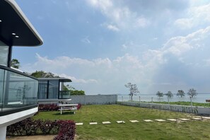 A modern house with a glass facade, a well-maintained lawn, and a view of the sea. - Saga Village Hotel & Resort Bintan By Zuzu (Bintan)