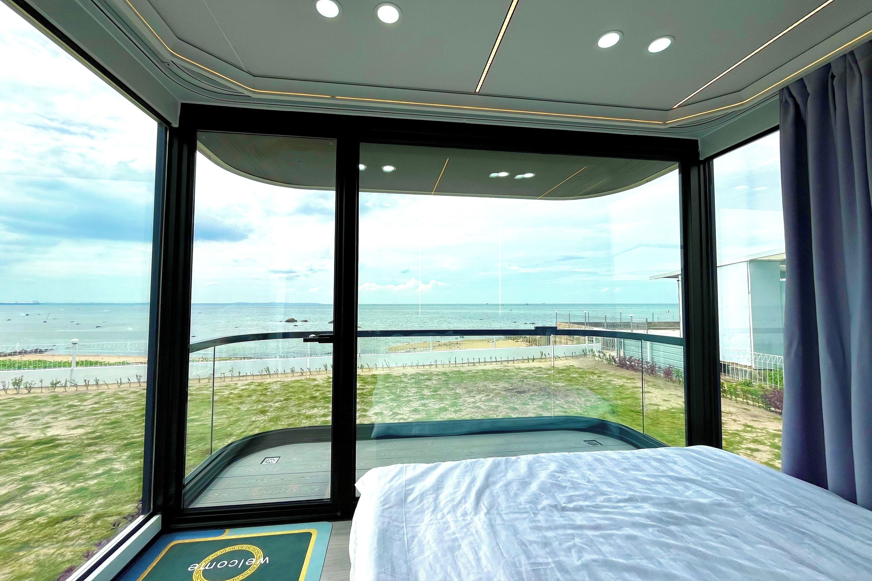 A modern hotel room with a large window offering a view of the beach and ocean.