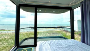 A modern hotel room with a large window offering a view of the beach and ocean. - Saga Village Hotel & Resort Bintan By Zuzu (Bintan)