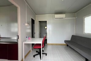 A compact room with a kitchenette, a dining table with a red chair, a grey sofa, and a small bathroom visible through an open door. - Saga Village Hotel & Resort Bintan By Zuzu (Bintan)