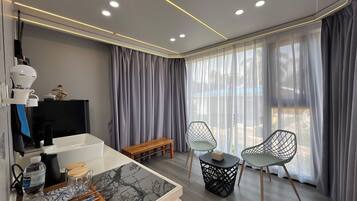 A modern room with a wooden bench, two chairs, a small table, a coffee maker, and a TV on a stand.