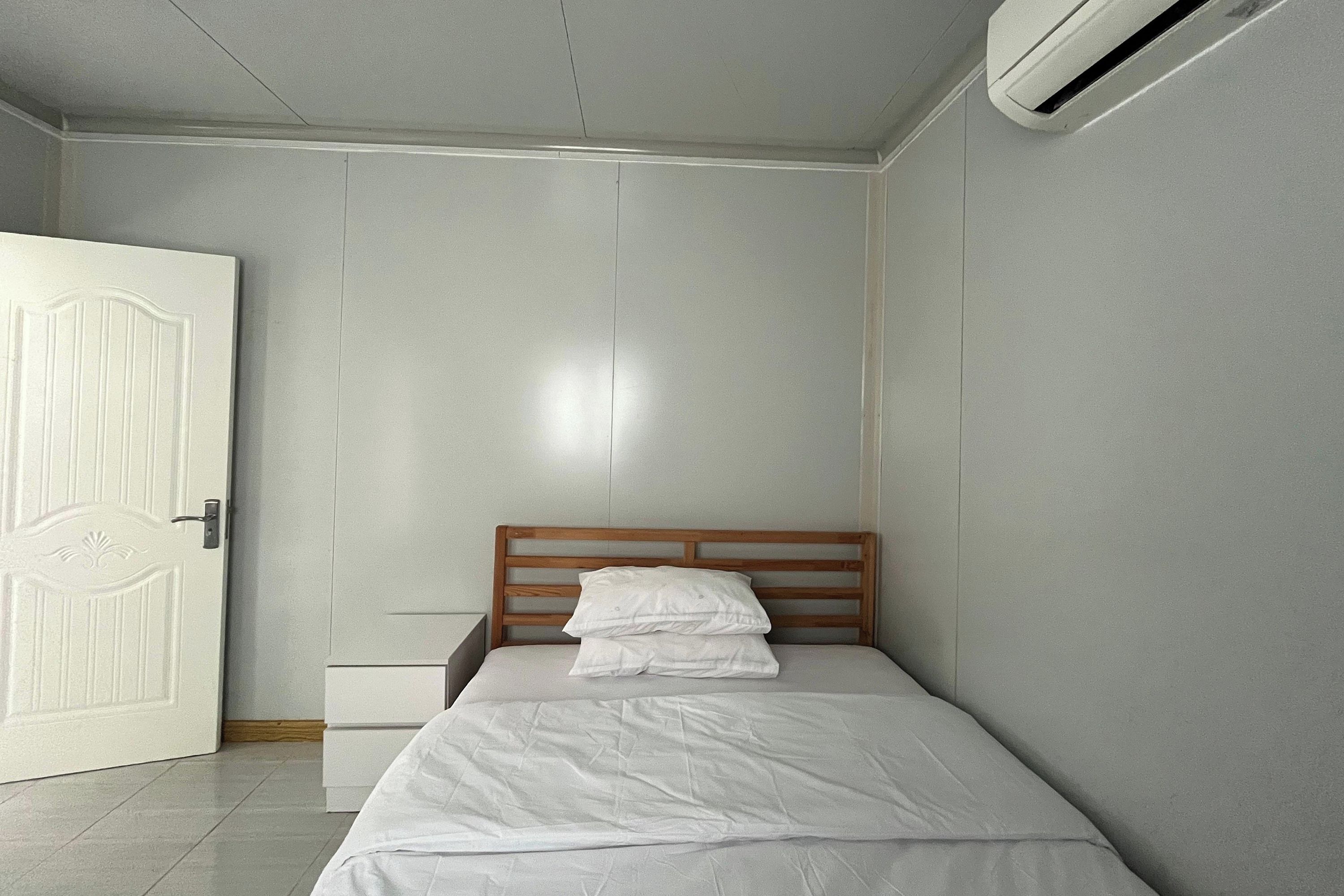 A bedroom with a wooden headboard, a white bedspread, and a white pillow.