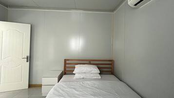 A bedroom with a wooden headboard, a white bedspread, and a white pillow.