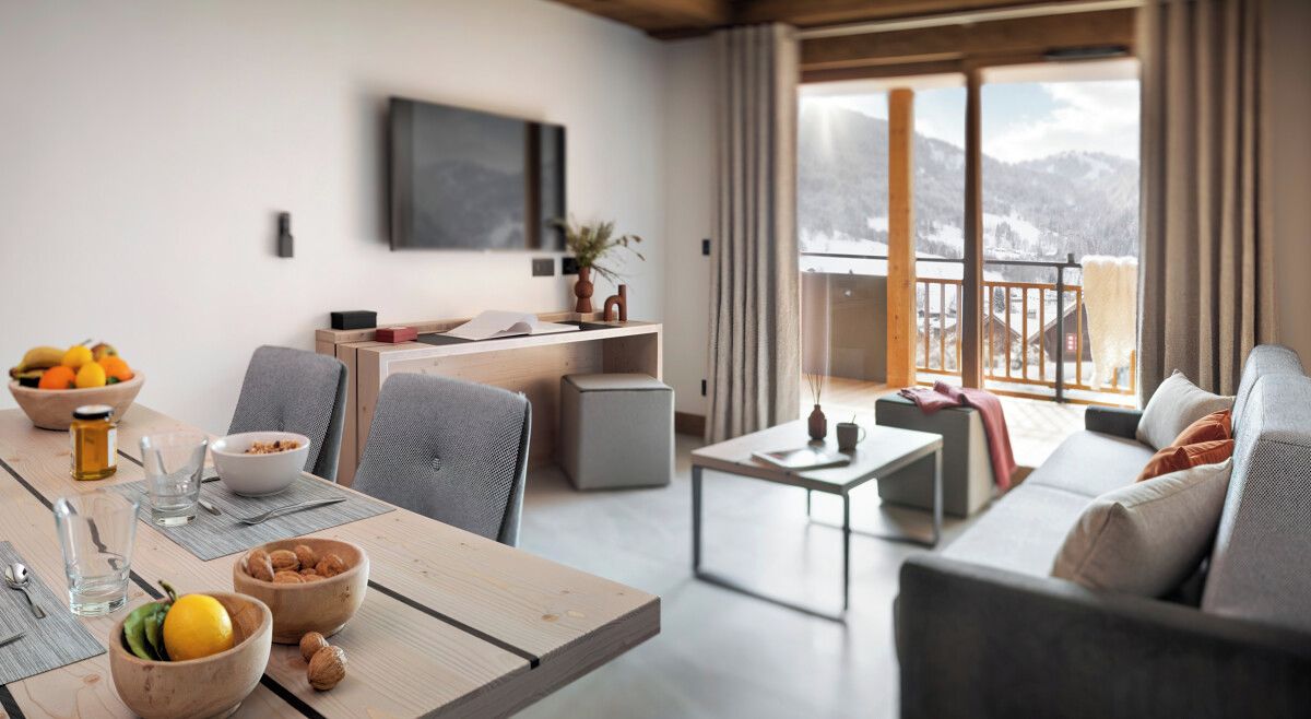 Un salon moderne avec une table à manger en bois, des canapés gris et un balcon offrant une vue sur la montagne.