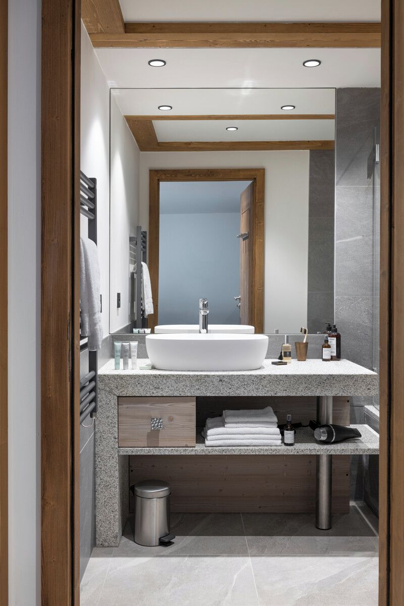 A modern bathroom with a large white sink, wooden beams, and a mirror.