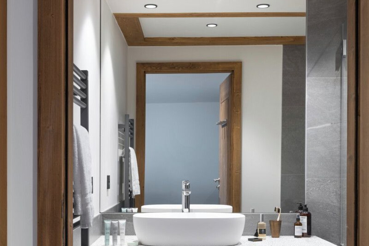 A modern bathroom with a large white sink, wooden beams, and a mirror.