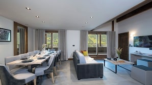 A modern living room with a dining area, large windows, and a flat-screen TV. - MGM Hôtels et Résidences - Hotel Laska (Les Contamines-Montjoie)