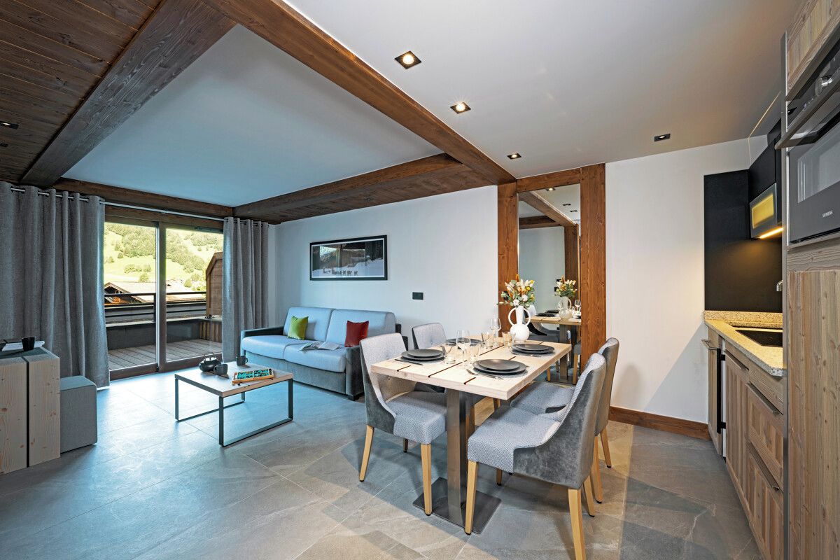 A modern living room with a dining area, wooden beams, a sofa, and a large window.