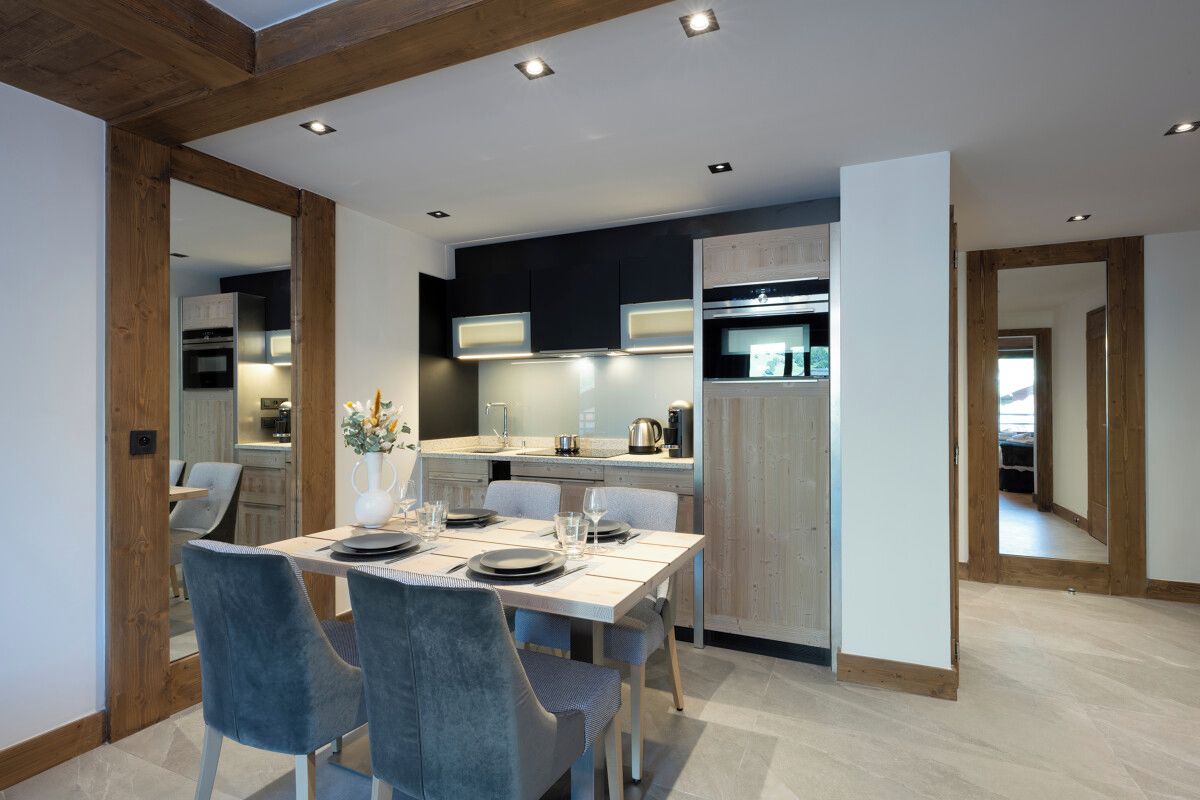 Une cuisine moderne avec des meubles de couleur sombre, un plafond en bois et un coin repas comprenant deux chaises et une table dressée pour deux personnes.
