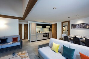 A modern living room with a sofa, coffee table, and a dining area with a table and chairs. - MGM Hôtels et Résidences - Hotel Laska (Les Contamines-Montjoie)