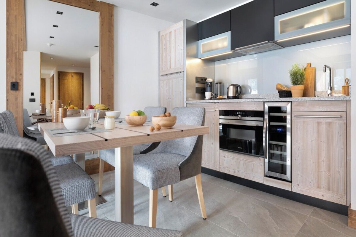 A modern kitchen with wooden cabinets, a built-in oven, and a dining area with a wooden table and chairs.
