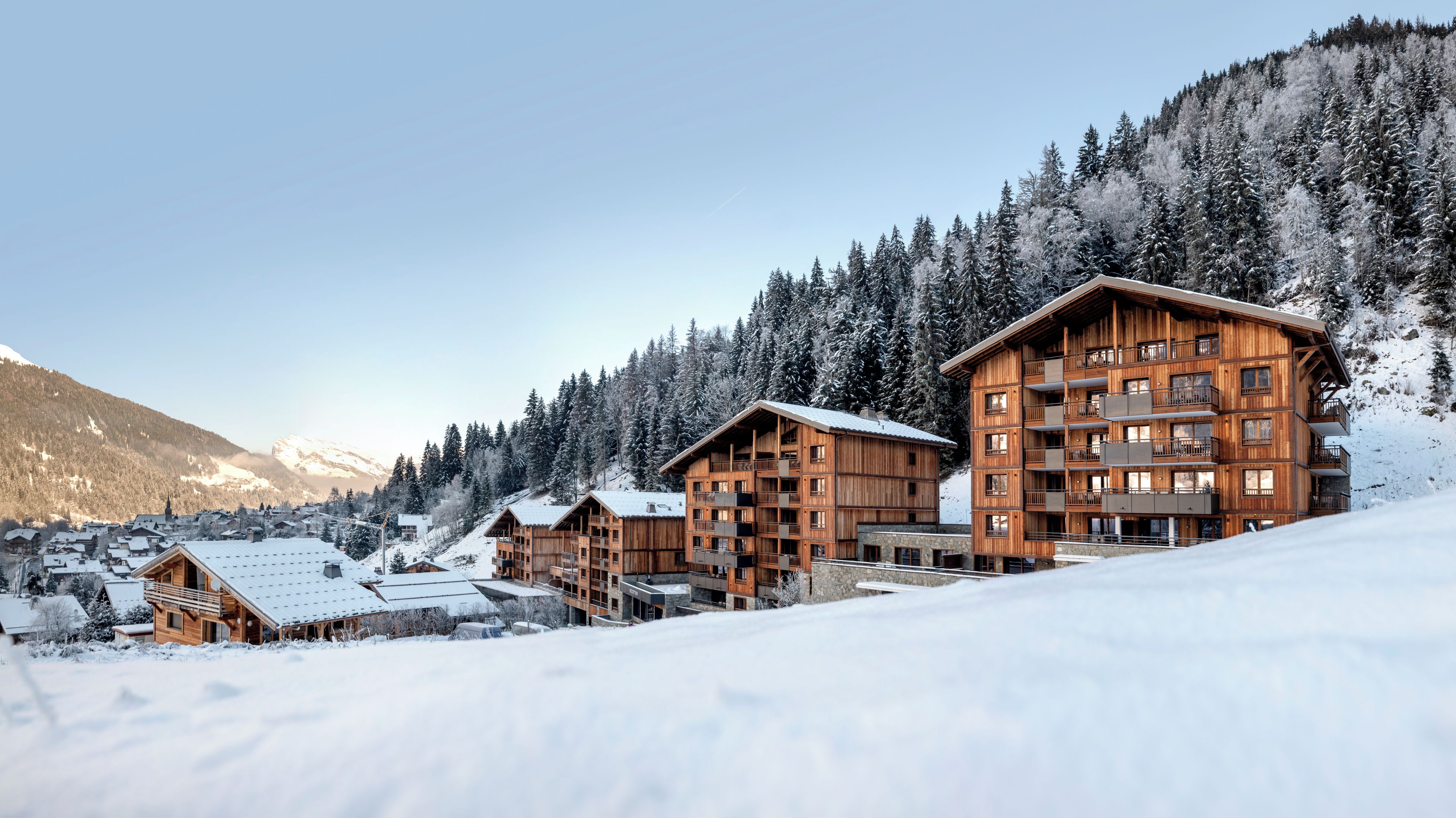 A wooden lodge with multiple balconies and a view of snow-covered trees and mountains.