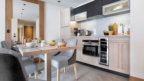 A modern kitchen with wooden cabinets, a built-in oven, and a dining area with a wooden table and chairs. - MGM Hôtels et Résidences - Hotel Laska (Les Contamines-Montjoie)