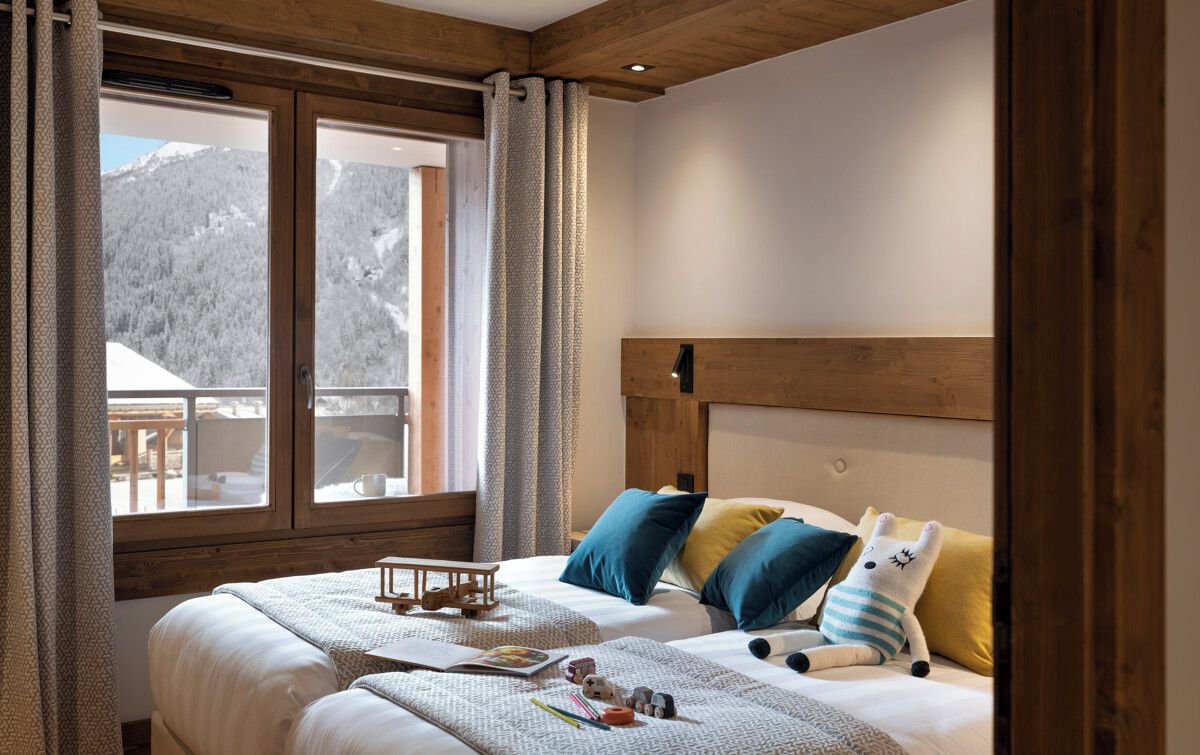 A bedroom with a wooden headboard, a large window with curtains, and a bed with pillows and a stuffed toy.