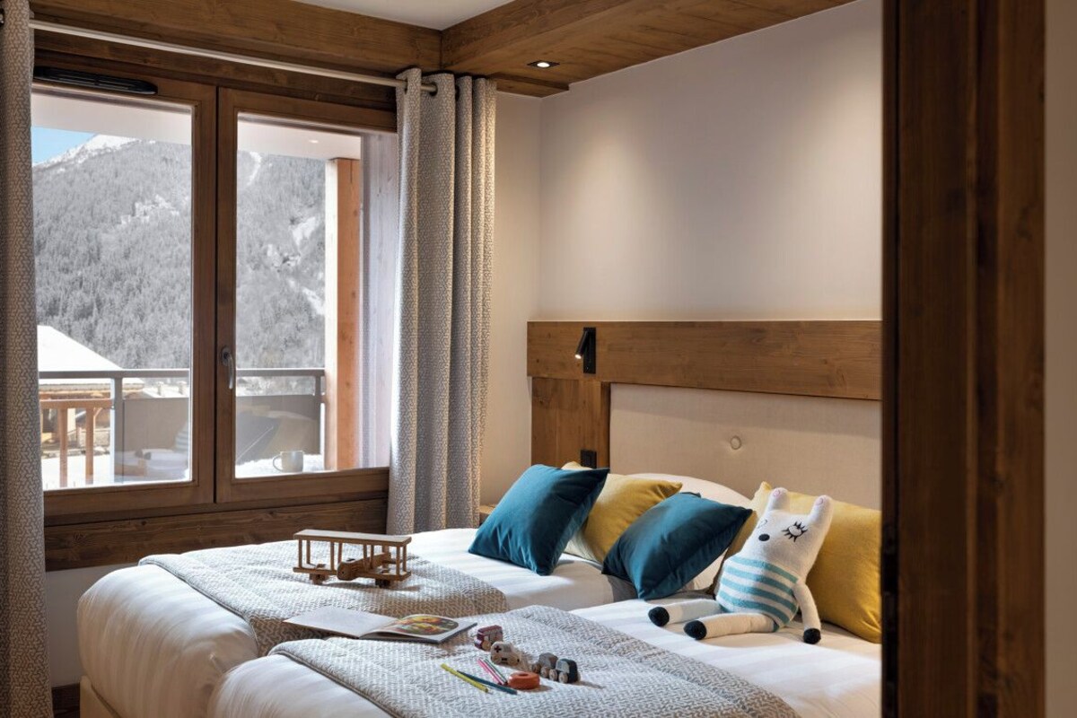 A bedroom with a wooden headboard, a large window with curtains, and a bed with pillows and a stuffed toy.