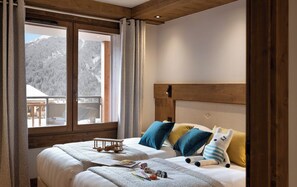 A bedroom with a wooden headboard, a large window with curtains, and a bed with pillows and a stuffed toy. - MGM Hôtels et Résidences - Hotel Laska (Les Contamines-Montjoie)