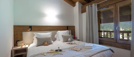 Une chambre à coucher avec une tête de lit en bois, un grand lit recouvert d’une couvre-lit à motifs, une table de chevet avec une lampe et une fenêtre donnant sur un paysage verdoyant.