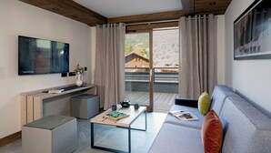 A modern living room with a flat-screen TV, a coffee table, a sofa, and a sliding glass door leading to a balcony. - MGM Hôtels et Résidences - Hotel Laska (Les Contamines-Montjoie)