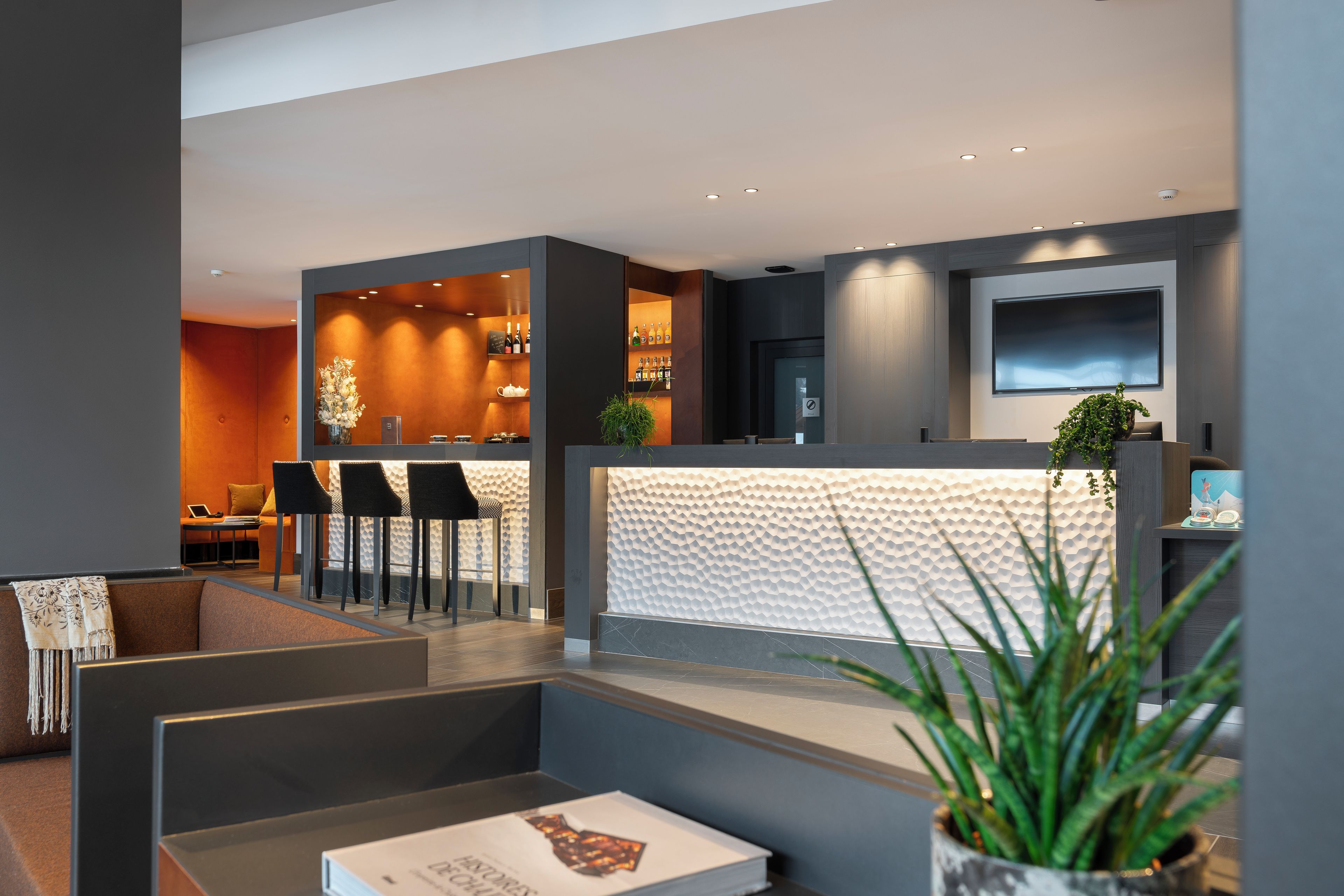 A modern hotel lobby with a reception desk, seating area, and bar.