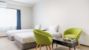 Een hotelkamer met twee enkele bedden, een bureau met stoel, een raam met gordijnen en een nachtkastje met een afstandsbediening en zakdoekjes.