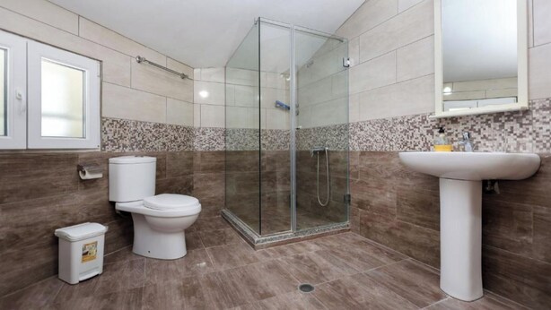 A modern bathroom with a glass-enclosed shower, a toilet, a sink, and a tiled backsplash. - Hotel Familja (Berat)