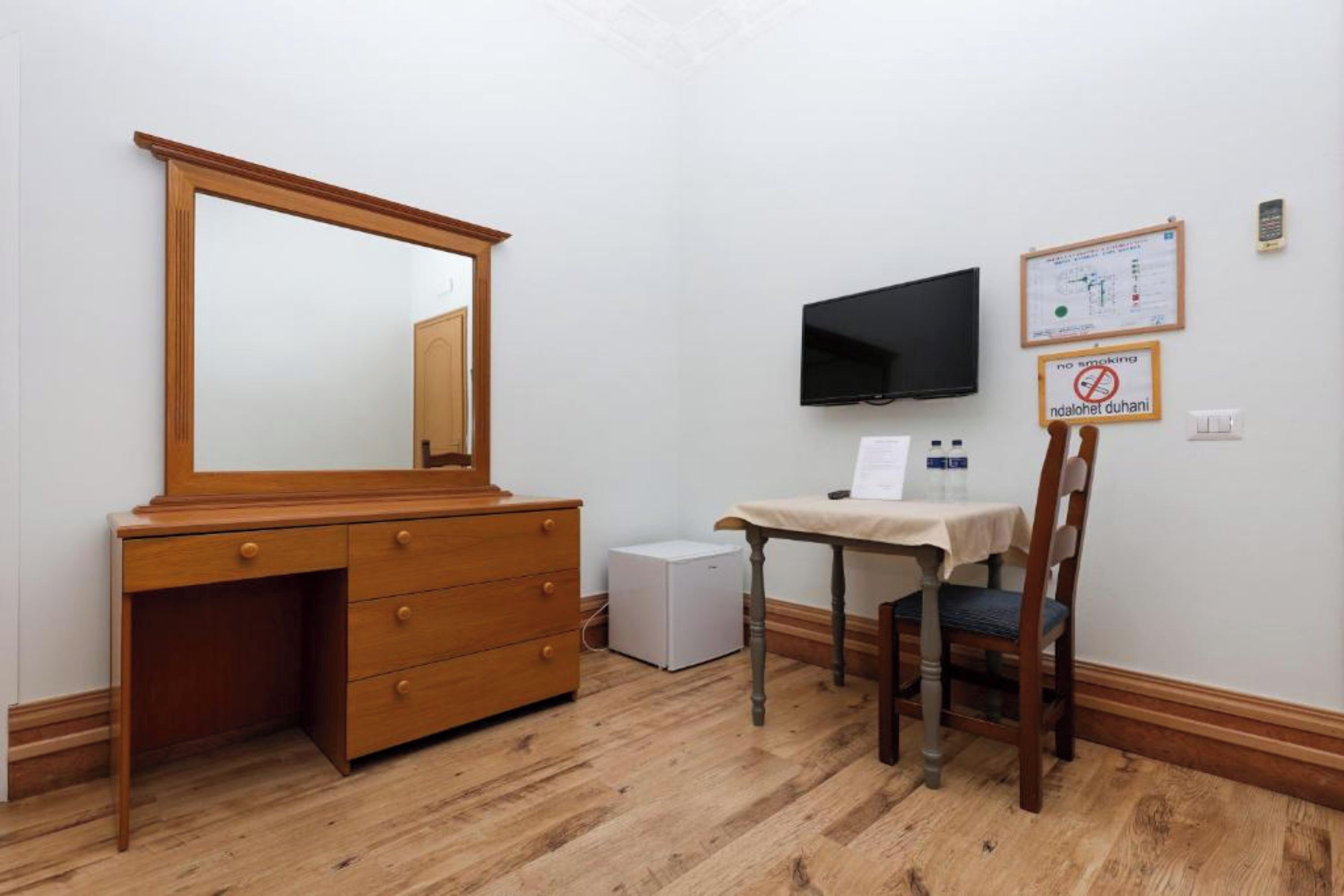Una habitación con un aparador de madera, un televisor montado en la pared, una mesita con una silla y un cartel de prohibido fumar.