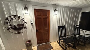 Une porte en bois ornée d’un motif circulaire en métal, une chaise en bois et une petite poubelle.