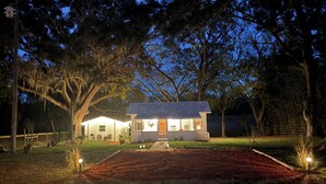 Une petite maison de plain-pied avec un porche, entourée d’arbres et d’une pelouse bien entretenue.