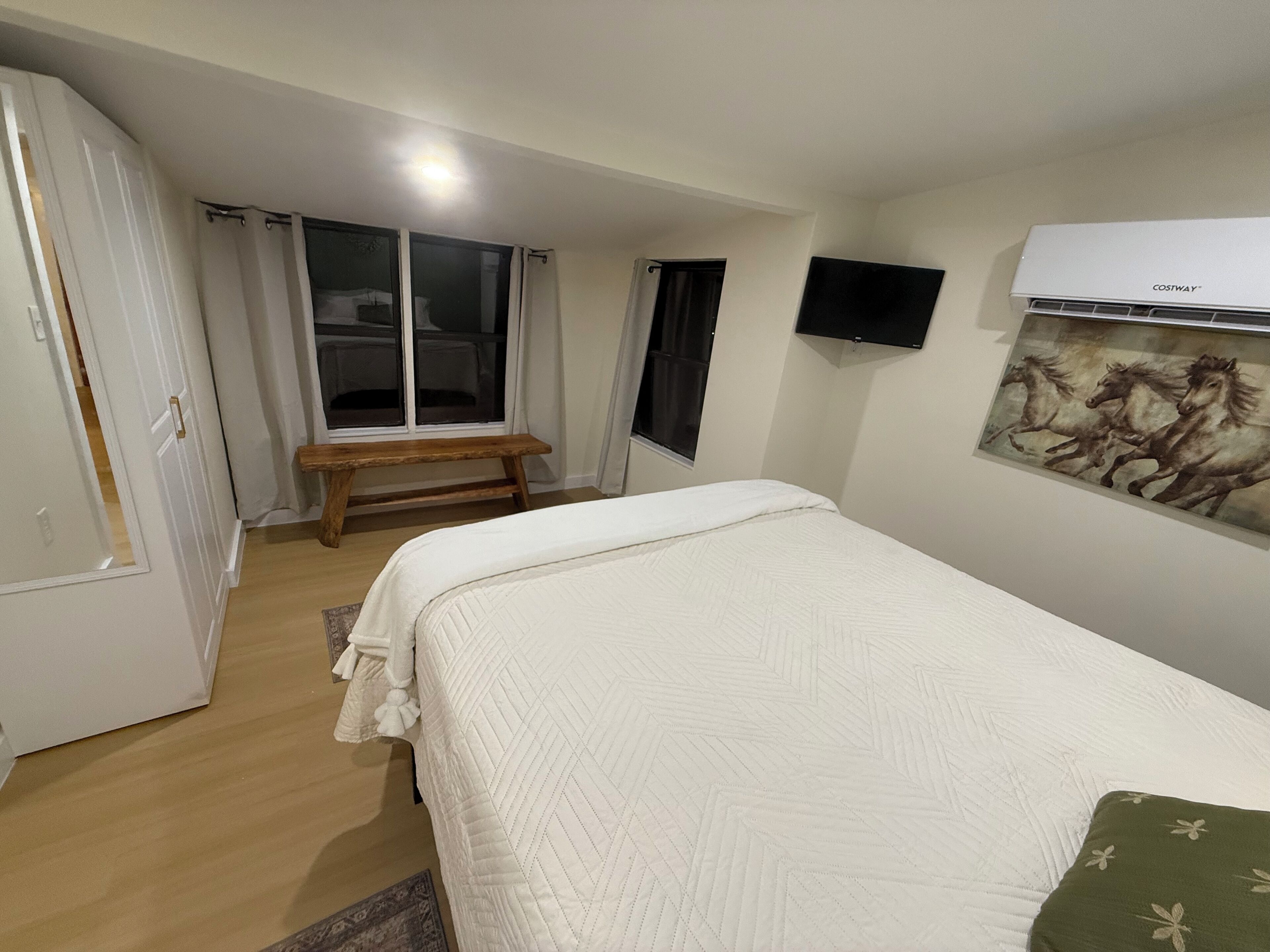 A bedroom with a bed, a bench, a TV, and an air conditioner.