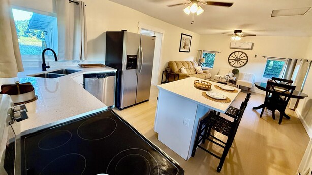 Une cuisine compacte équipée d’un réfrigérateur, d’une cuisinière et d’un évier. On y trouve également un coin repas avec une table et des chaises, ainsi qu’un ventilateur de plafond.