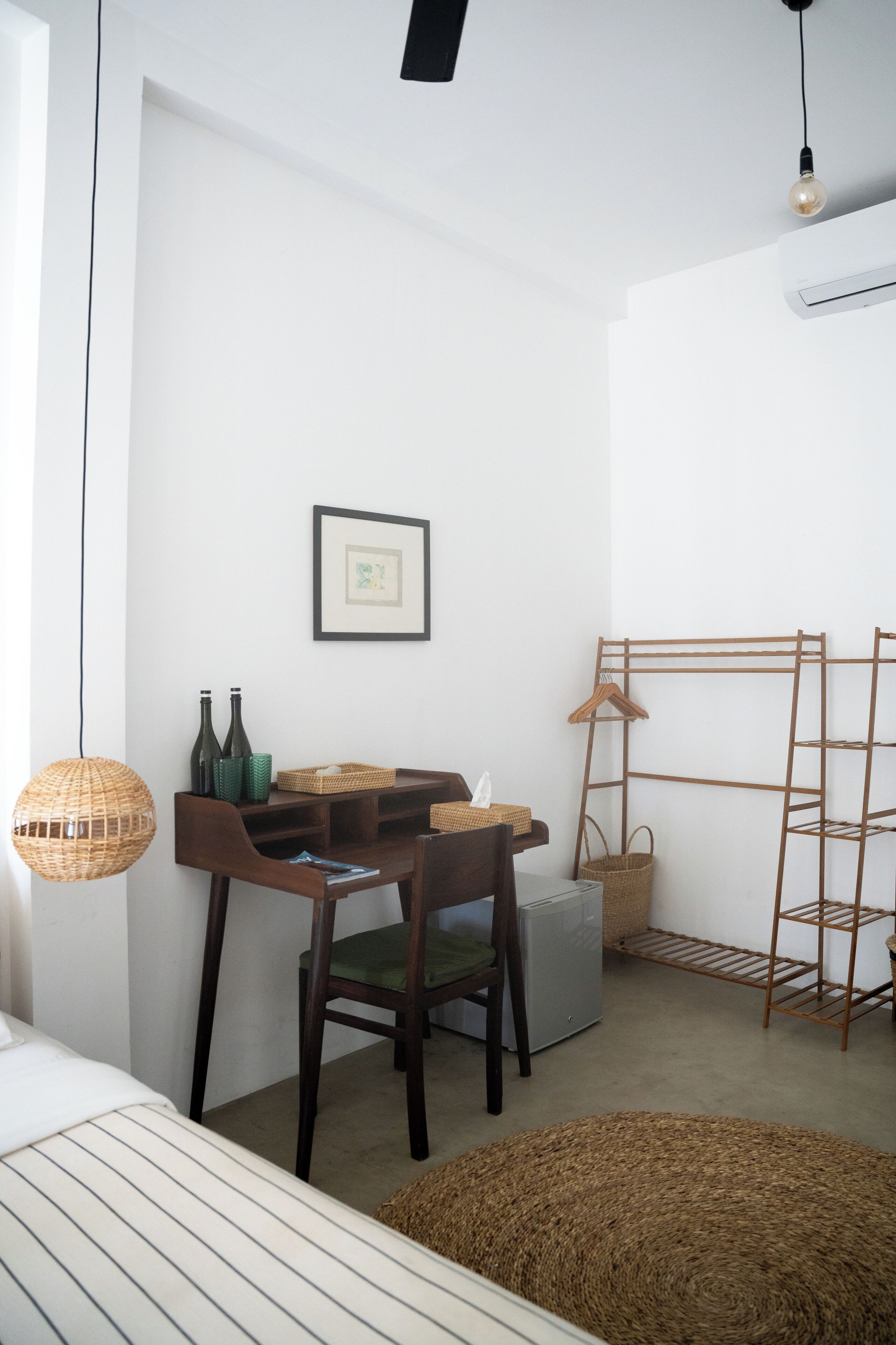 Ein Zimmer mit einem Bett, einem Schreibtisch mit Stühlen, einer Hängelampe, einem gerahmten Bild und einem Wäscheständer.