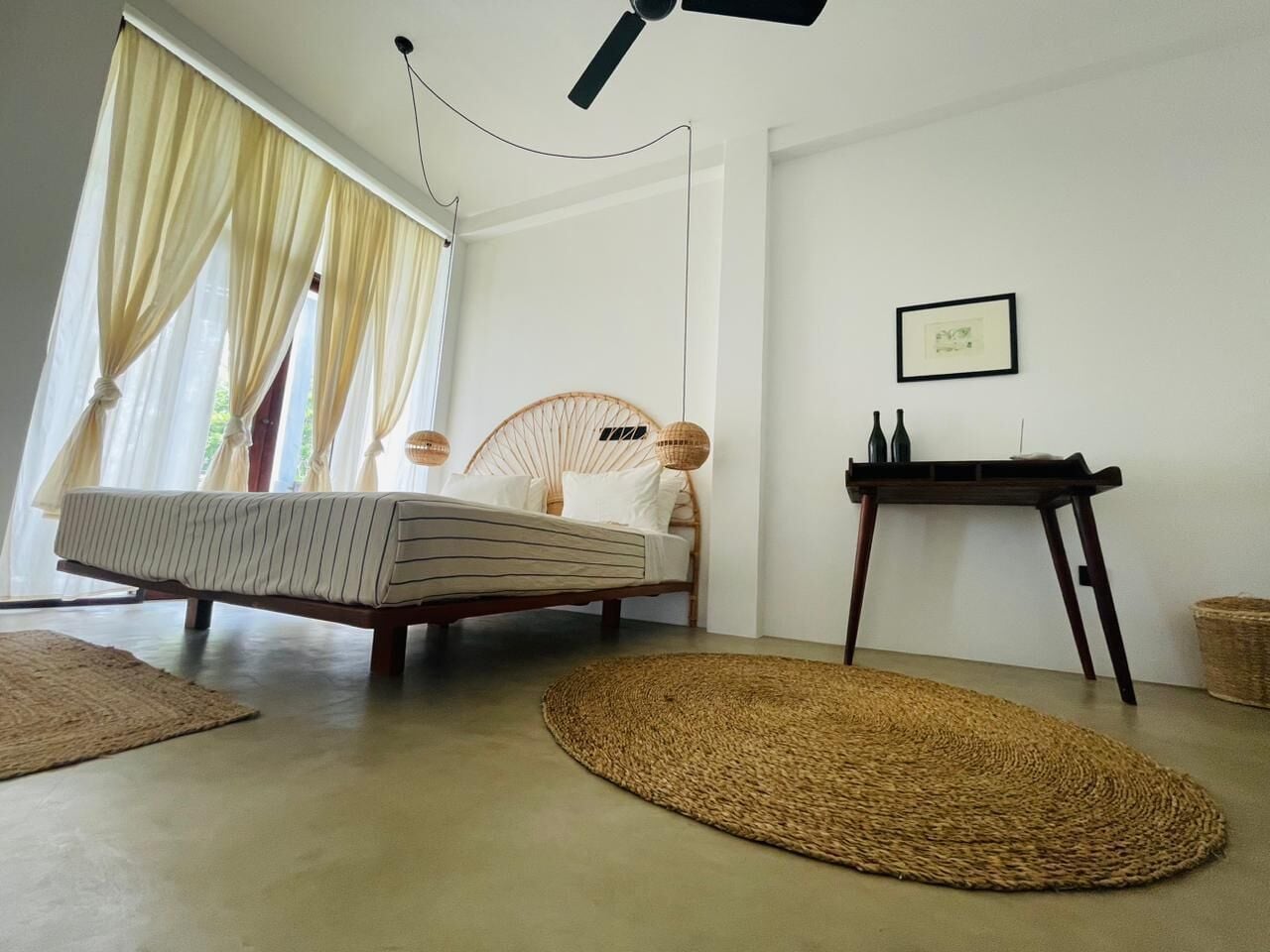 A room with a bed, a wicker chair, a small table, and a woven rug.