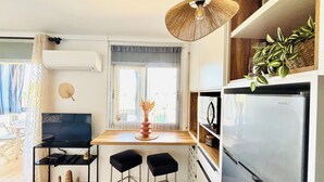 A compact kitchen with a modern refrigerator, a dining table with two stools, a hanging light fixture, and a window with curtains. - Lorena. Renovated Apartment with Terrace & Parking (Roses)