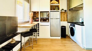 A compact kitchen with a microwave, refrigerator, and washing machine. There is a small bar area with stools and a television. - Lorena. Renovated Apartment with Terrace & Parking (Roses)