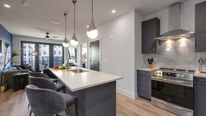 Une cuisine moderne dotée d’un îlot central, d’appareils électroménagers en acier inoxydable et de luminaires suspendus.